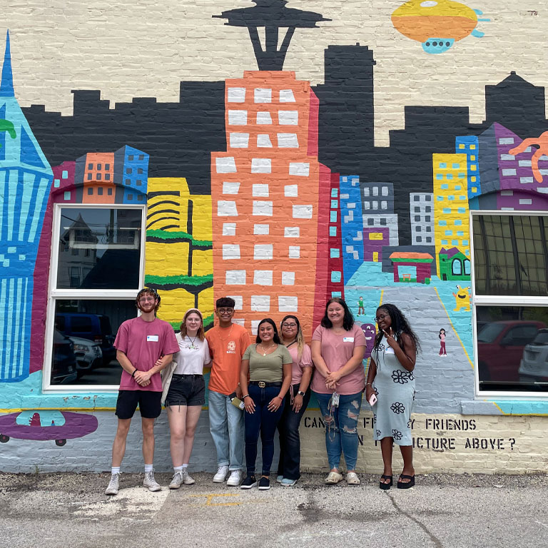 A group of students stand in front of a mural