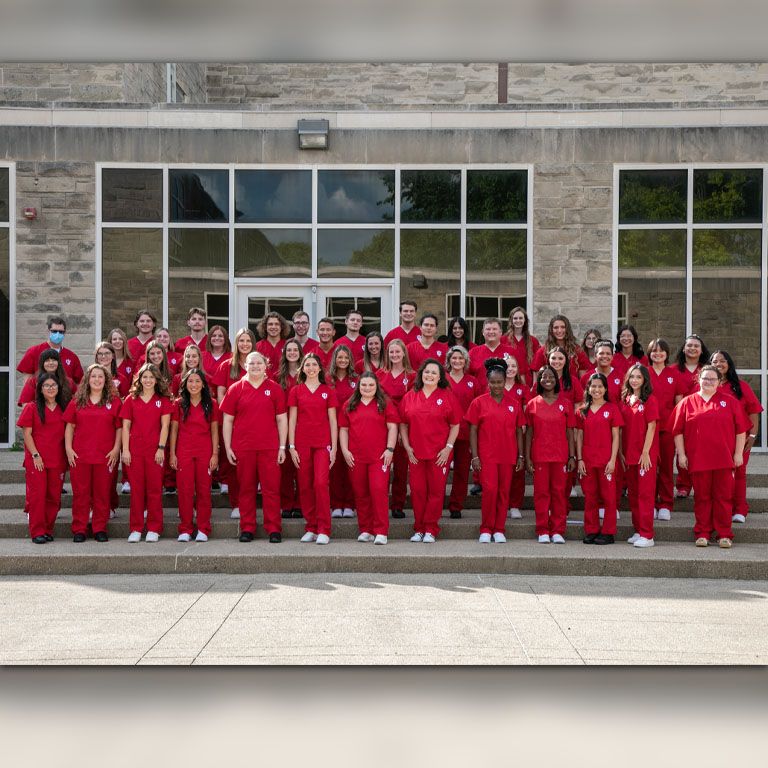 A large group of men and women pose in red scrubs.