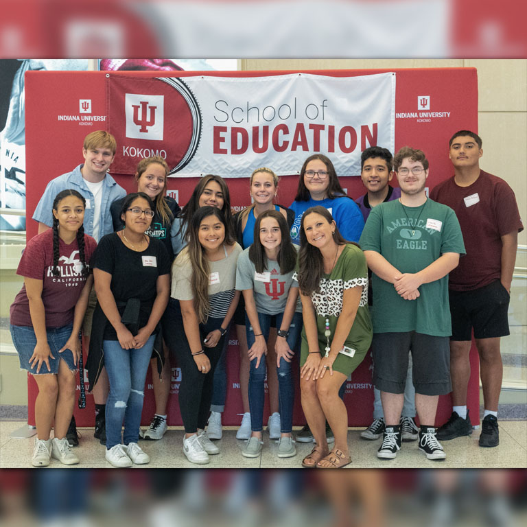 A group of nine women and four men pose in front of a red IU backdrop.