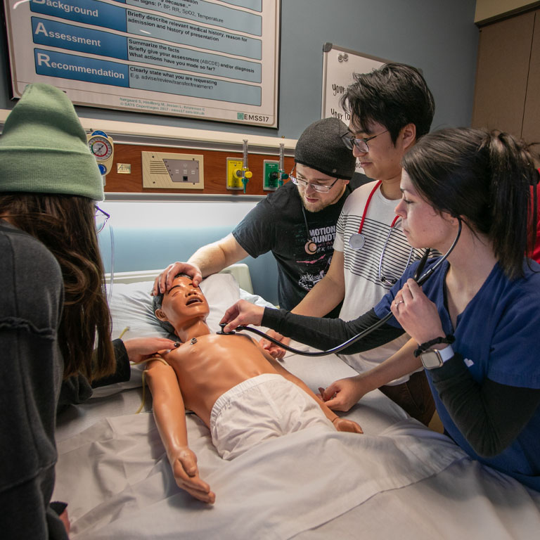 Two men and two women gather around a nursing simulation mannequin.