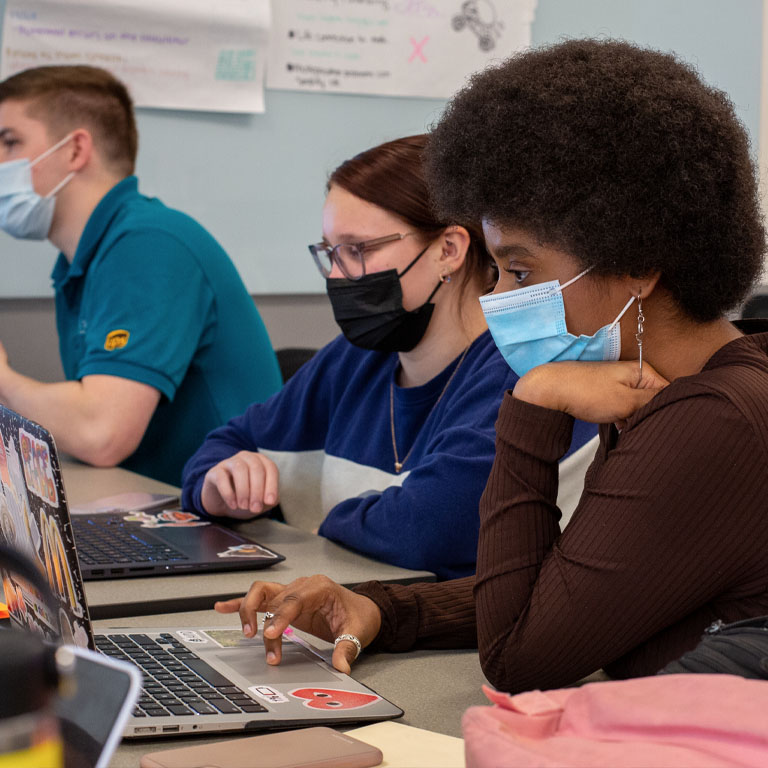 Two people in masks look at a laptop