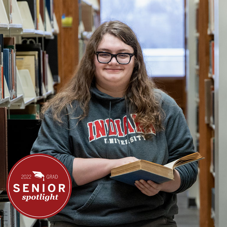 A woman stands between shelves in a library