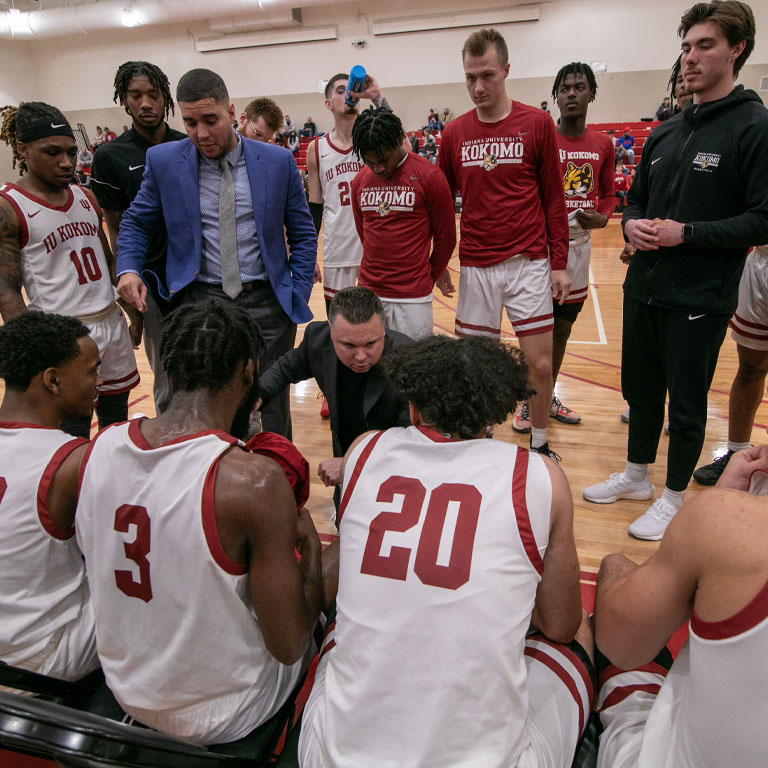 Men's basketball players huddle around the coach during a time out