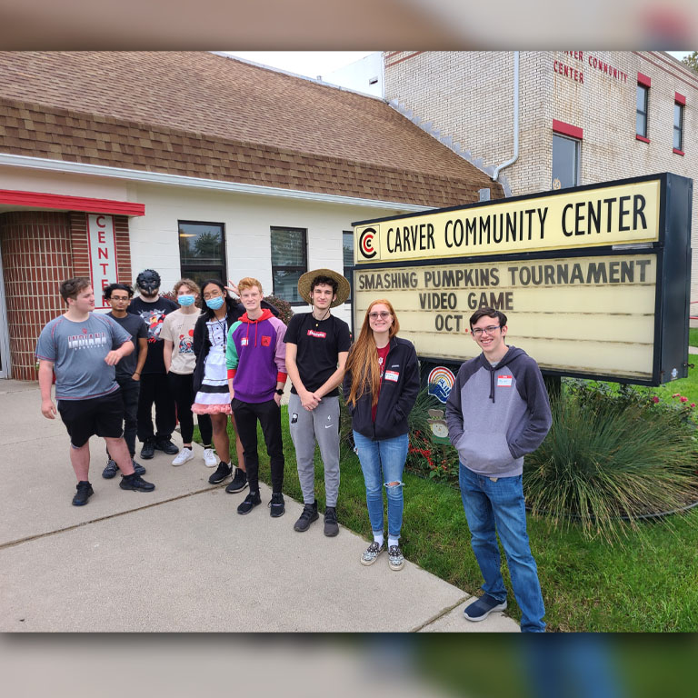Nine people pose in front of the Carver Center sign