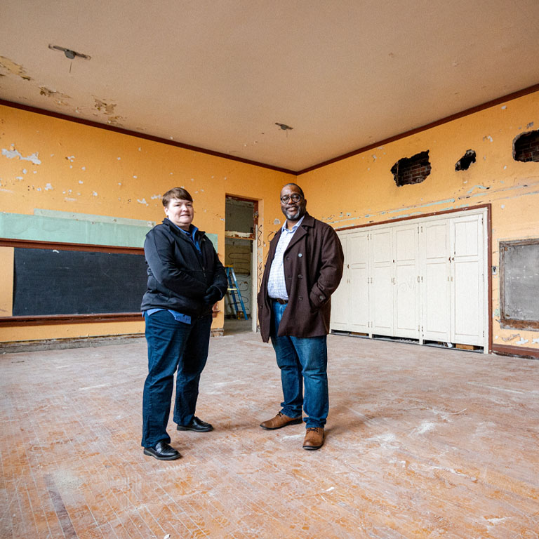 A woman and a man stand inside an old classroom