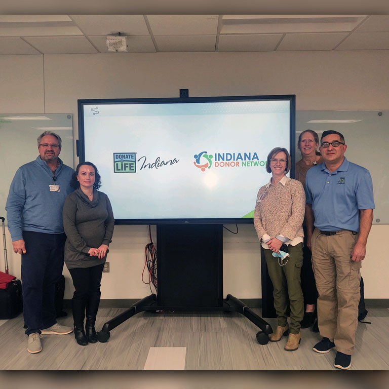 Five people stand by a screen with the Indiana Donor Network logo on it