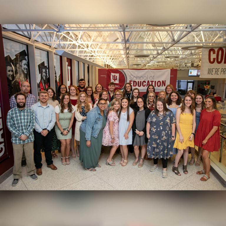 A group of people stand in front of a red background