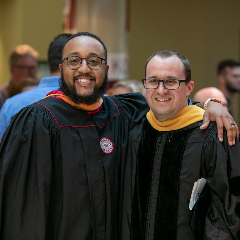 two graduate students in robe and masters hood