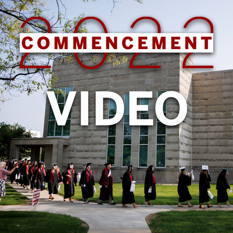 A line of graduates walk past a limestone building