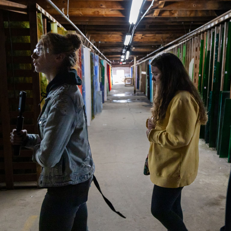 Two women walk through Kokomo Opalescent Glass.