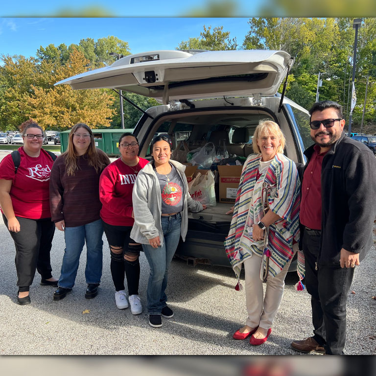 Five women and one man stand in front of an open van with household supplies.