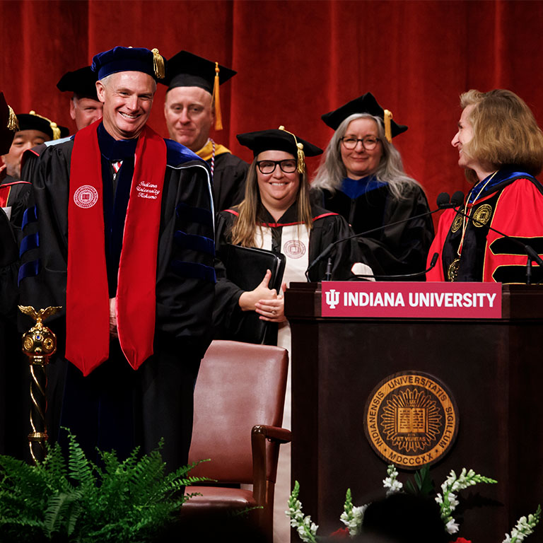 A group of people in academic regalia smile during a celebration.