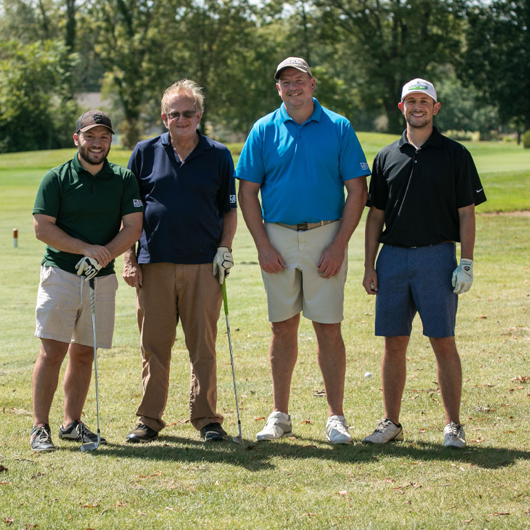 A group of four men pose on a golf course.