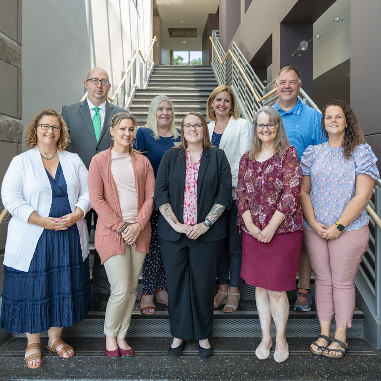 Seven women and two men stand on in rows on a staircase
