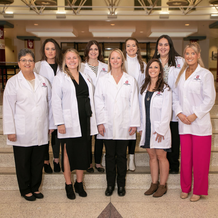 Nine women pose in white lab coats