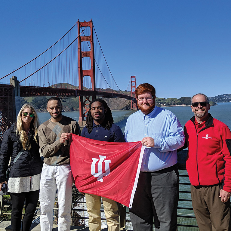 Five people hold an IU flag in front of the Golden Gate bridge.