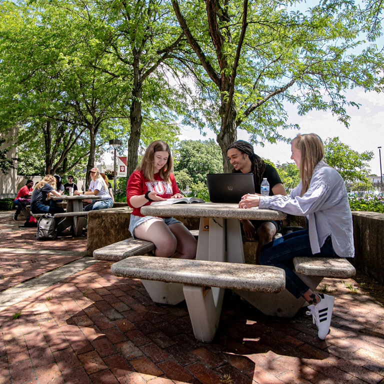Three students sit at an outdoor table