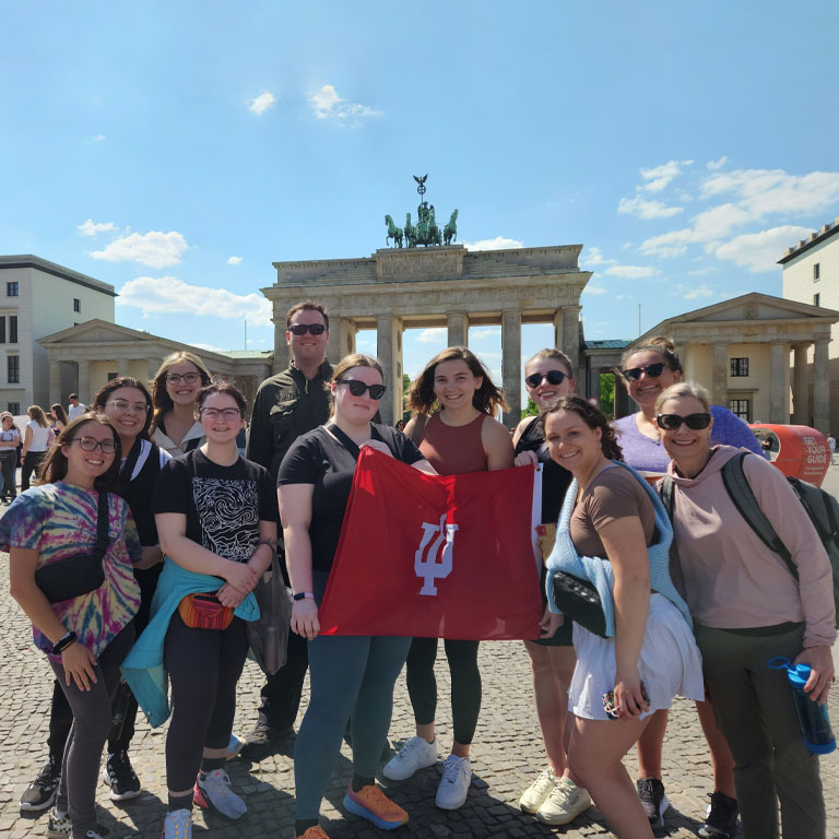 A group of people hold an IU flag in front of the Brandenburg Gates