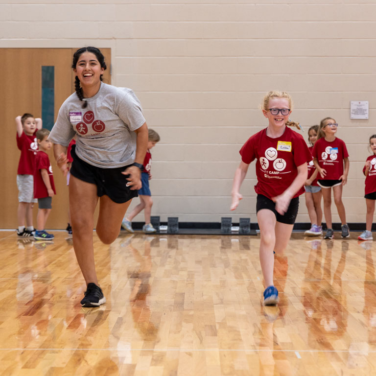 A woman and a girl run in a gym