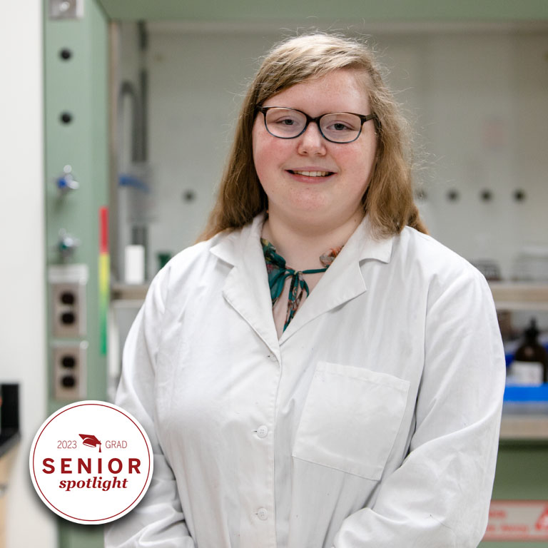 A woman in a white lab coat poses in a lab.