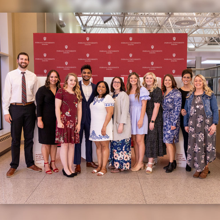 A group of students pose for a picture in front of large white letters IUK