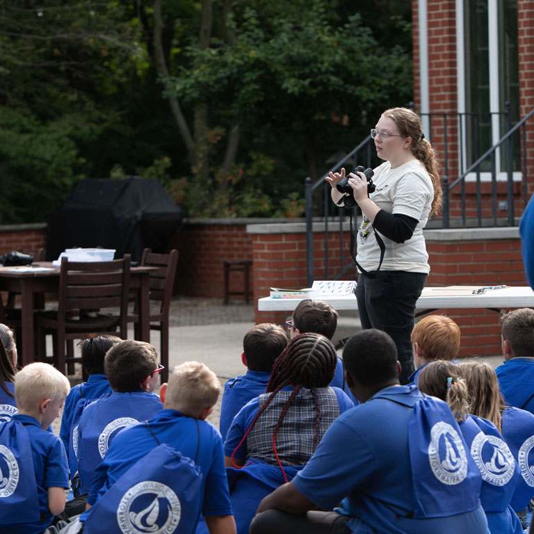 A woman holds binoculars in front of a group of children
