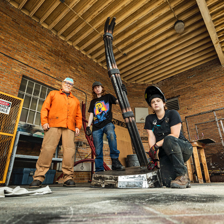 Three people pose with a metal sculpture