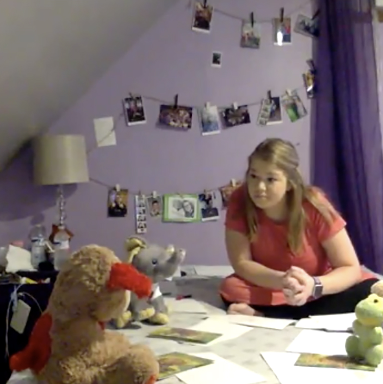 Screen shot of a woman sitting on a bed with stuffed animals