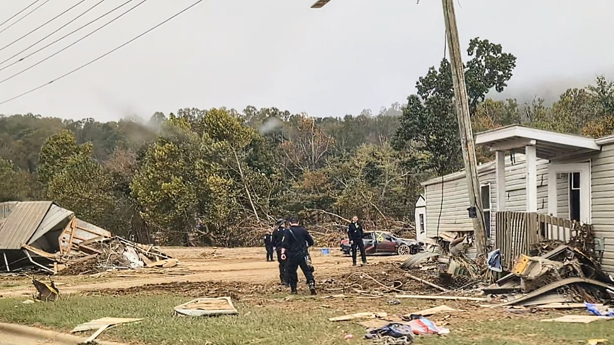 Emergency personnel in a debris-filled yard survey hurricane damage to a home.