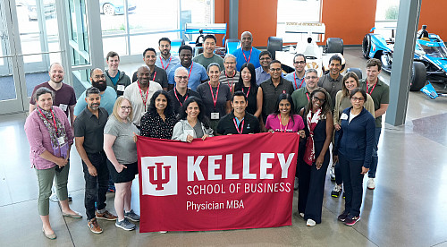 A group stands in a building lobby holding a banner with the name of the IU Kelley School of Business
