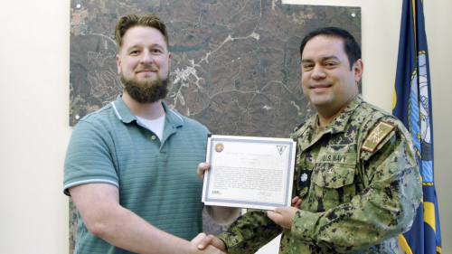 Two men shake hands while holding a certificate between them