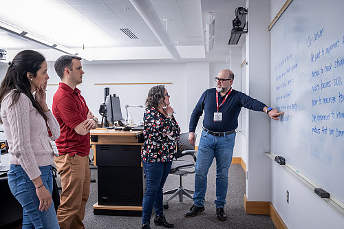 students listen as an instructor gestures towards a whiteboard