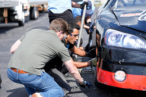 Two men change a race car tire on a race track