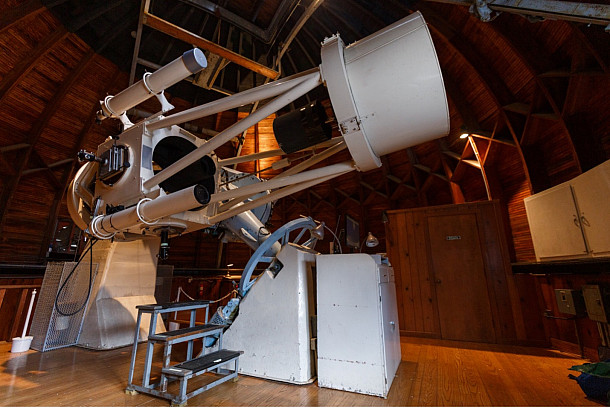 A large observatory telescope sits beneath a wooden dome