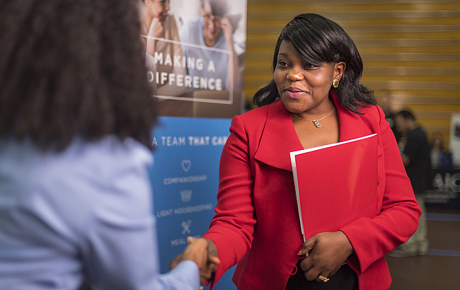 A woman in a red blazer shakes hands with an employer at a job fair