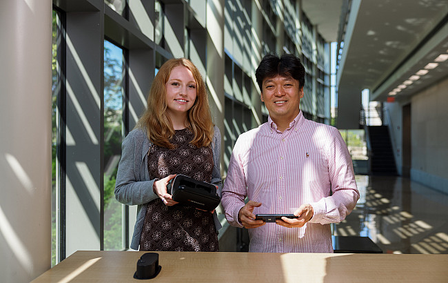 A man and a woman hold a VR headset and a cell phone in a sunny hallway