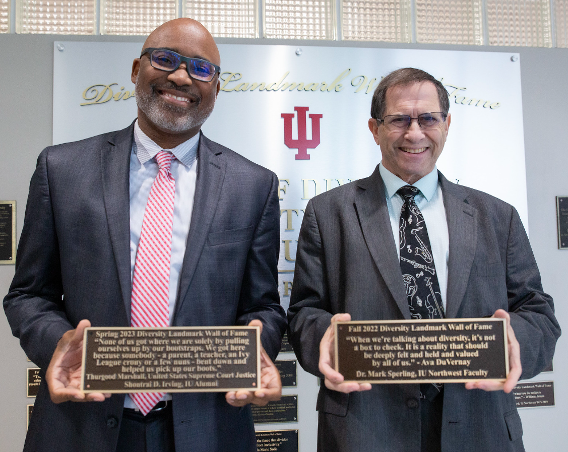 Two men holds plaques in front of a wall.