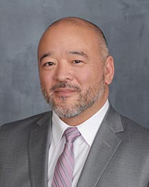 A man in a suit smiles for a headshot.