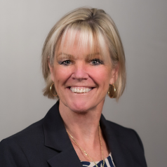 A woman smiling in front of a gray background.