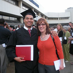 A man in a graduation gown stands with a woman, both smiling.