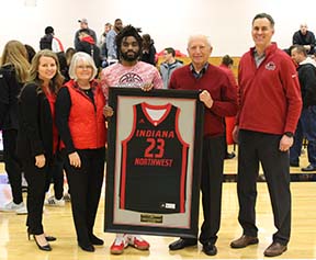 A group of people in a gym stand holding a framed jersey.