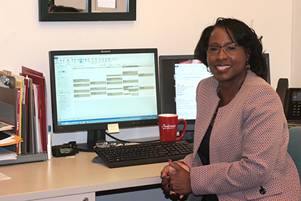 A woman at a desk smiles in front of computers.