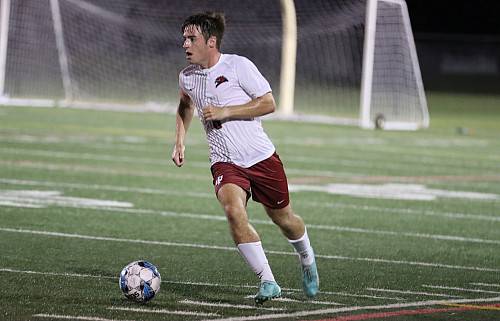 A man kicks a soccer ball on a field.