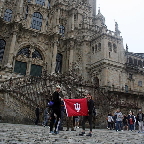 Two students hold a flag outside an old building.