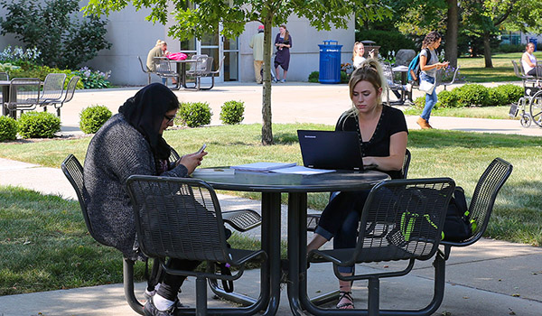 Two students sit at a table outside.