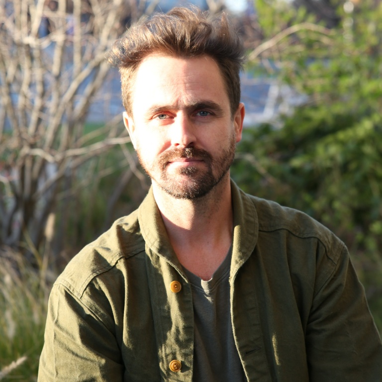 A male faculty member smiling while sitting outside with the sun on his face.