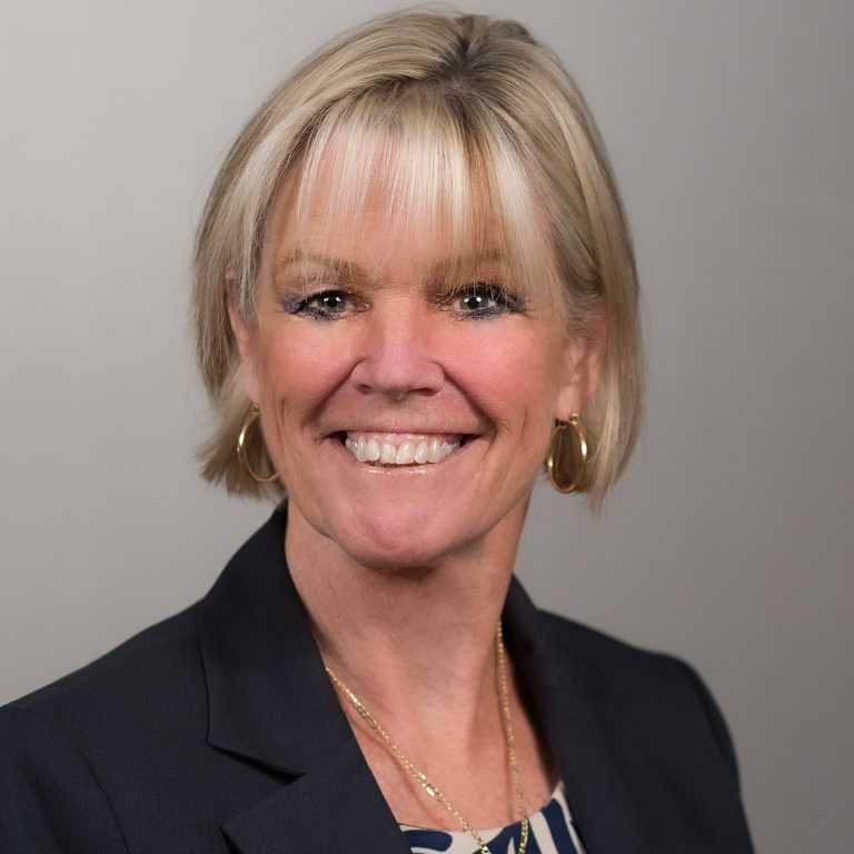 A female faculty member smiles in front of a gray background.
