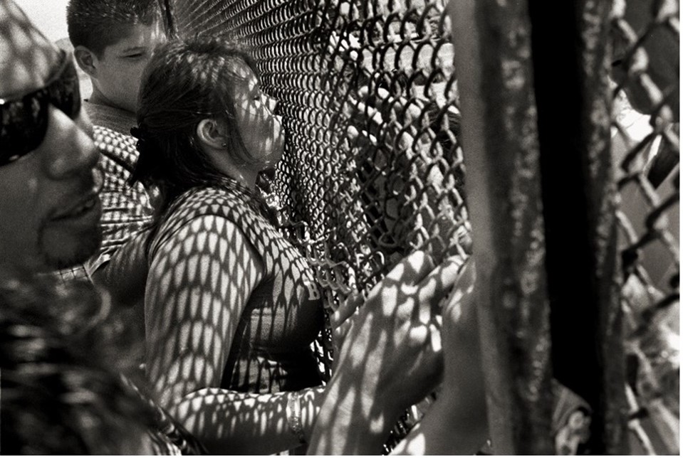 A woman kisses through a fence in a black-and-white photo.