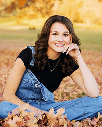 Aleigha Williams sits on ground, cross-legged, in a pile of crisp autumn leaves