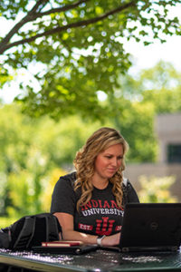 Julia Titus in her IU T-shirt, sitting outside and working on her laptop